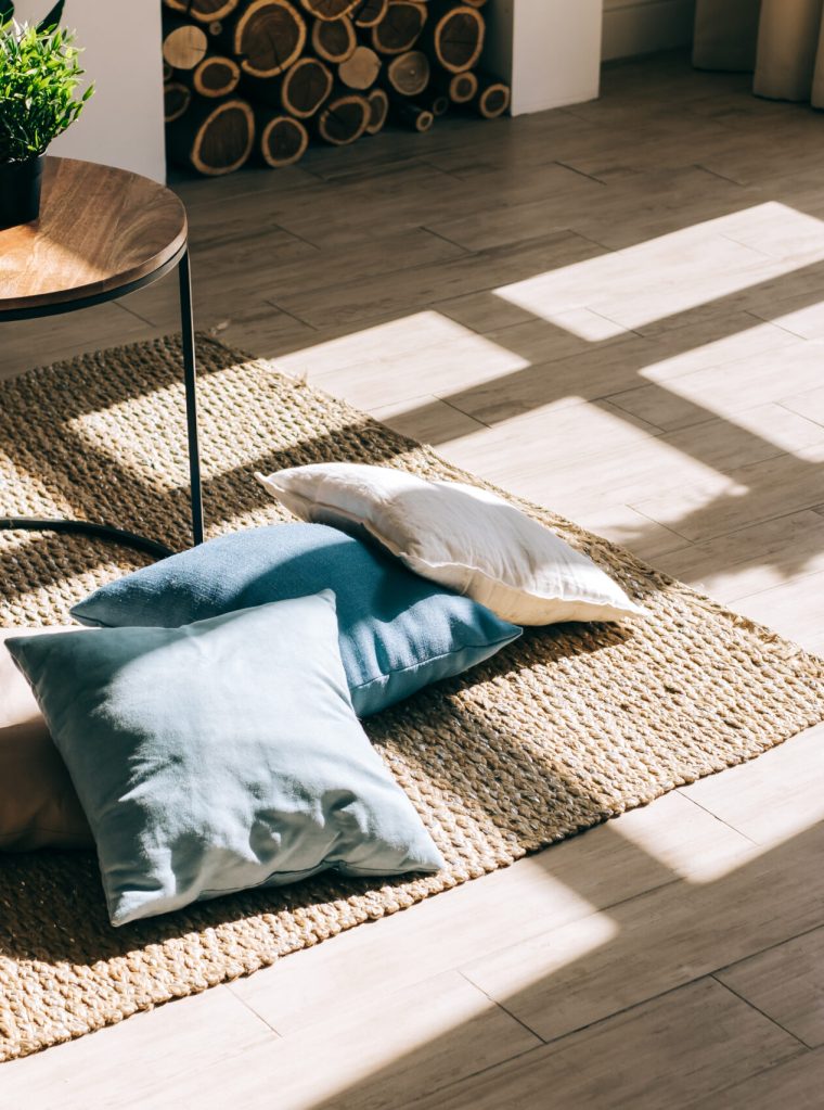 Interior of bright living room in scandinavian style with coffee table and pillows on the floor, big shadow from window on the floor.