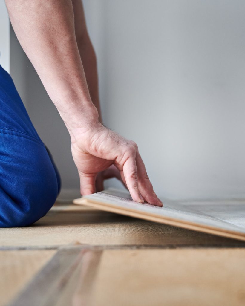 Male hands laying laminate wood plank on floor underlayment. Close up of man construction worker installing laminate timber flooring in apartment under renovation. Hardwood floor renovation concept.